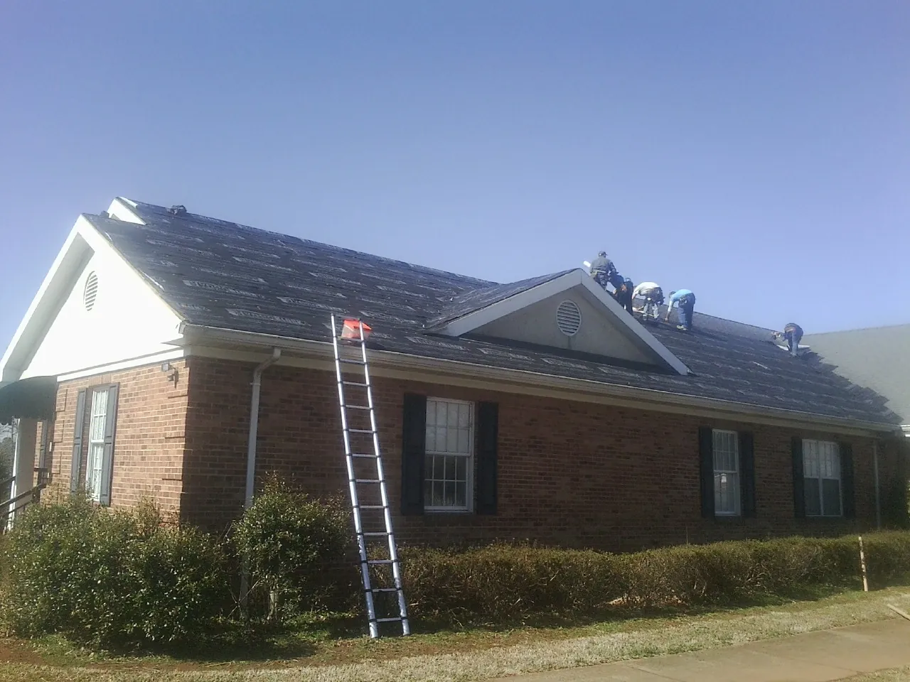 Crew tearing shingles off a brick ranch roof with a ladder set — Metal Roof Repair work by our crew in Abbeville